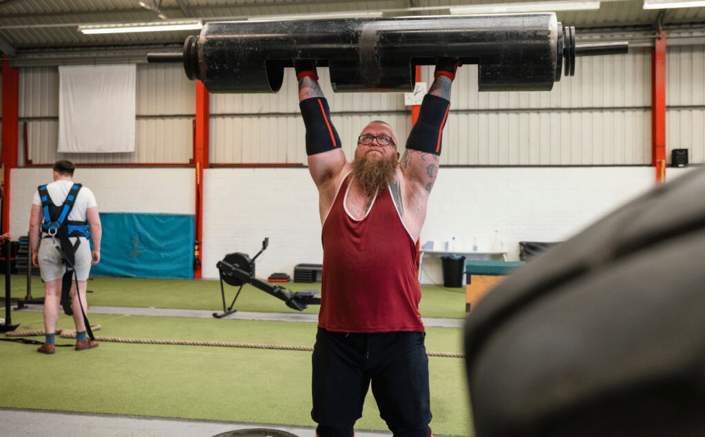 man lifting a strongman log above his head