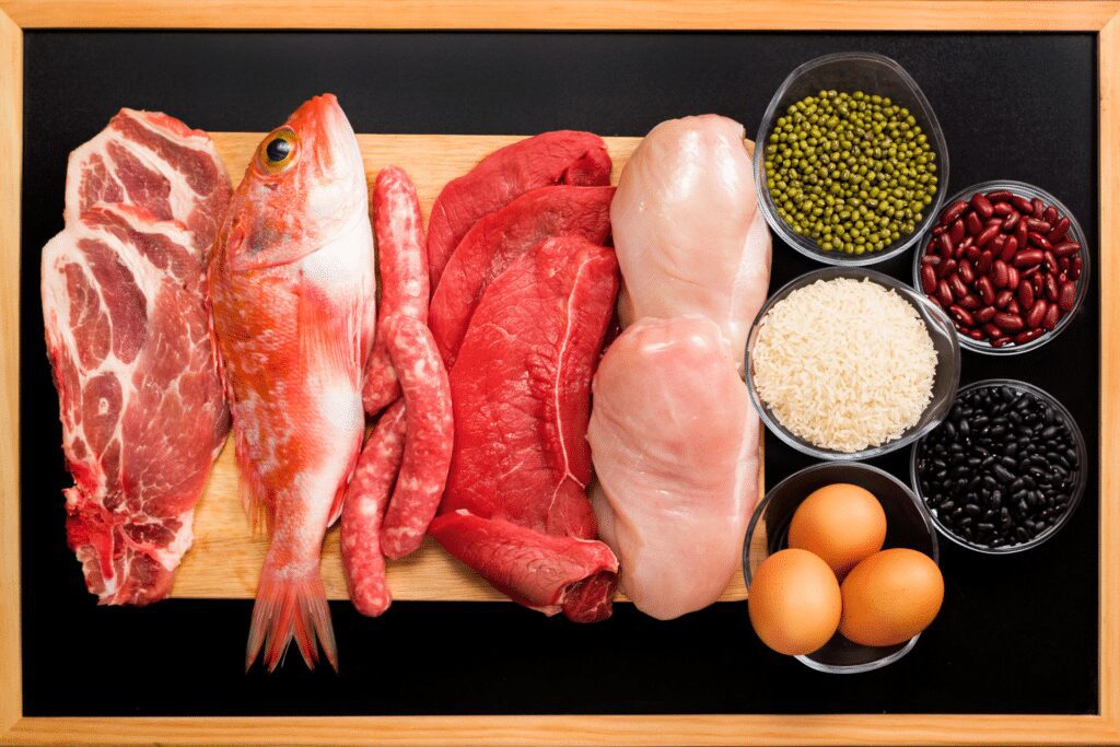 fish, steak, chicken, and other protein rich foods in bowls and on a cutting board
