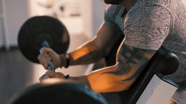 man with grey shirt and tattoos doing preacher curls