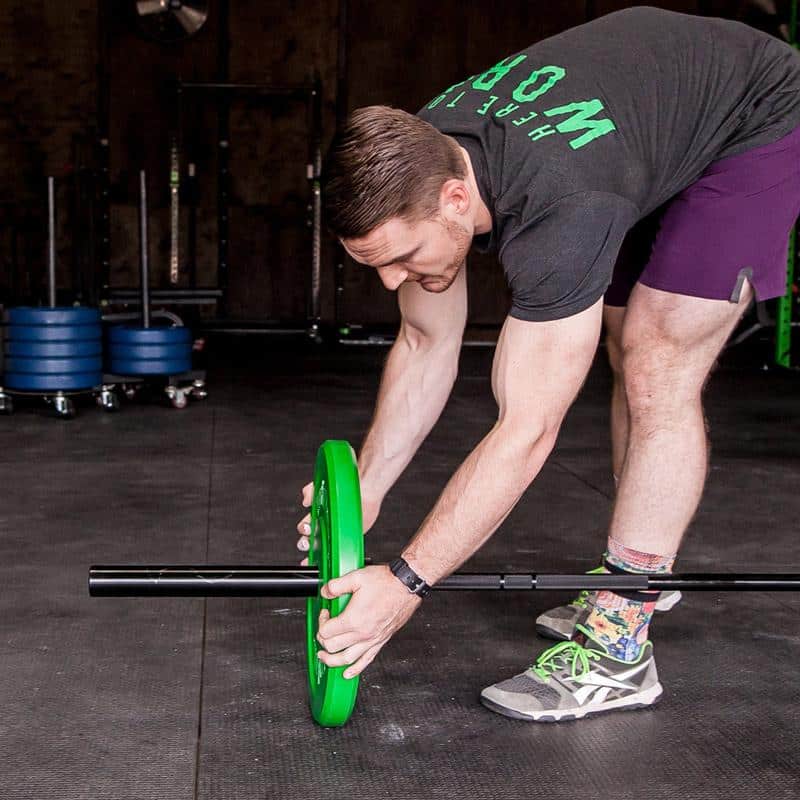 man loading barbell with green plates