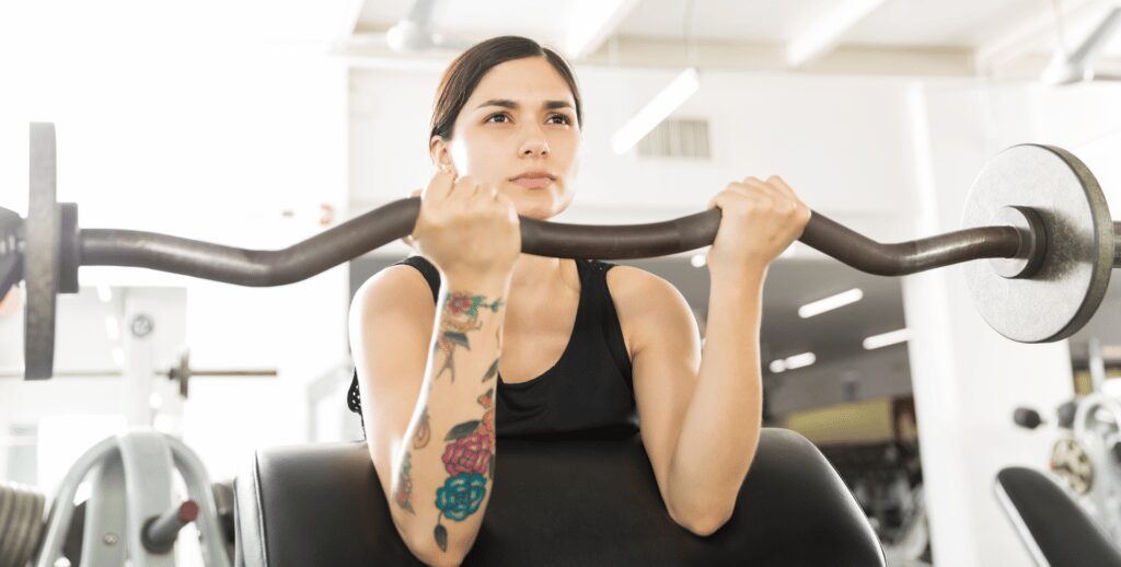 woman with colorful flower tattoos doing ez bar preacher curls