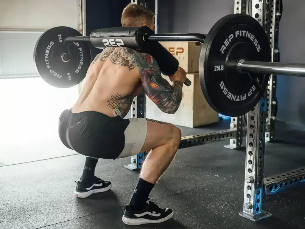 man with tattoos squats outside squat rack