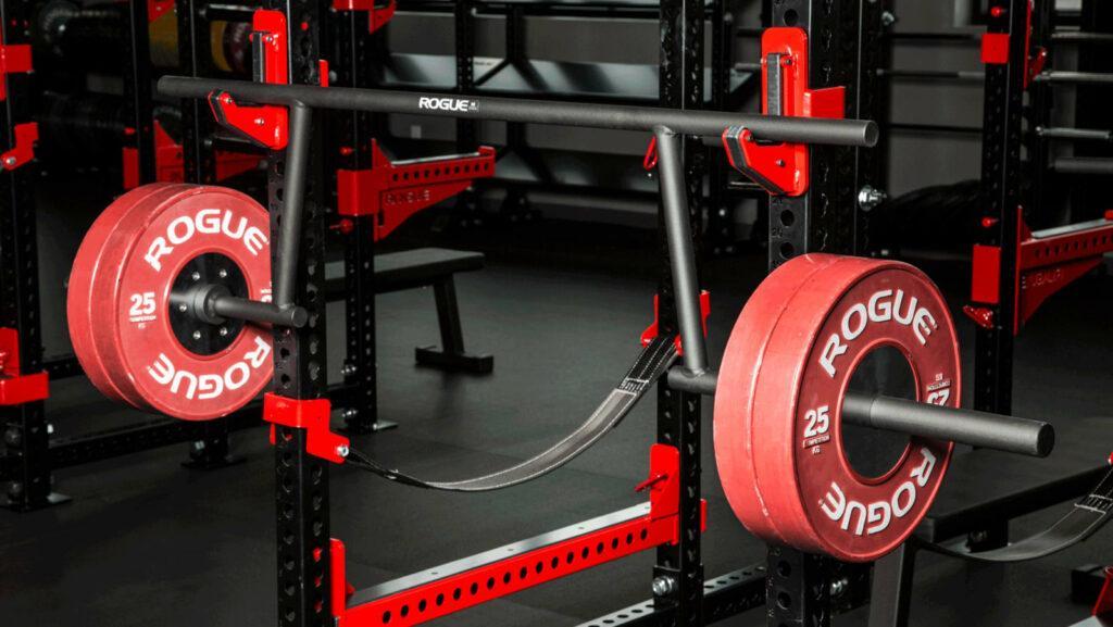 cambered barbell in rack with red bumper plates on it
