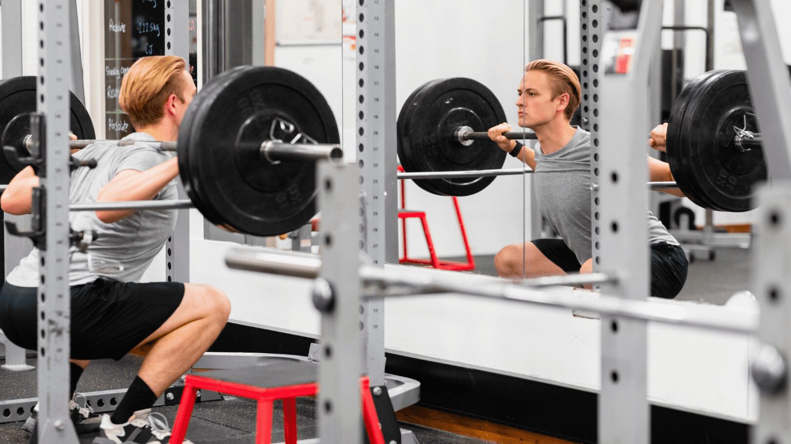 man squatting in rack while looking into mirror at his form